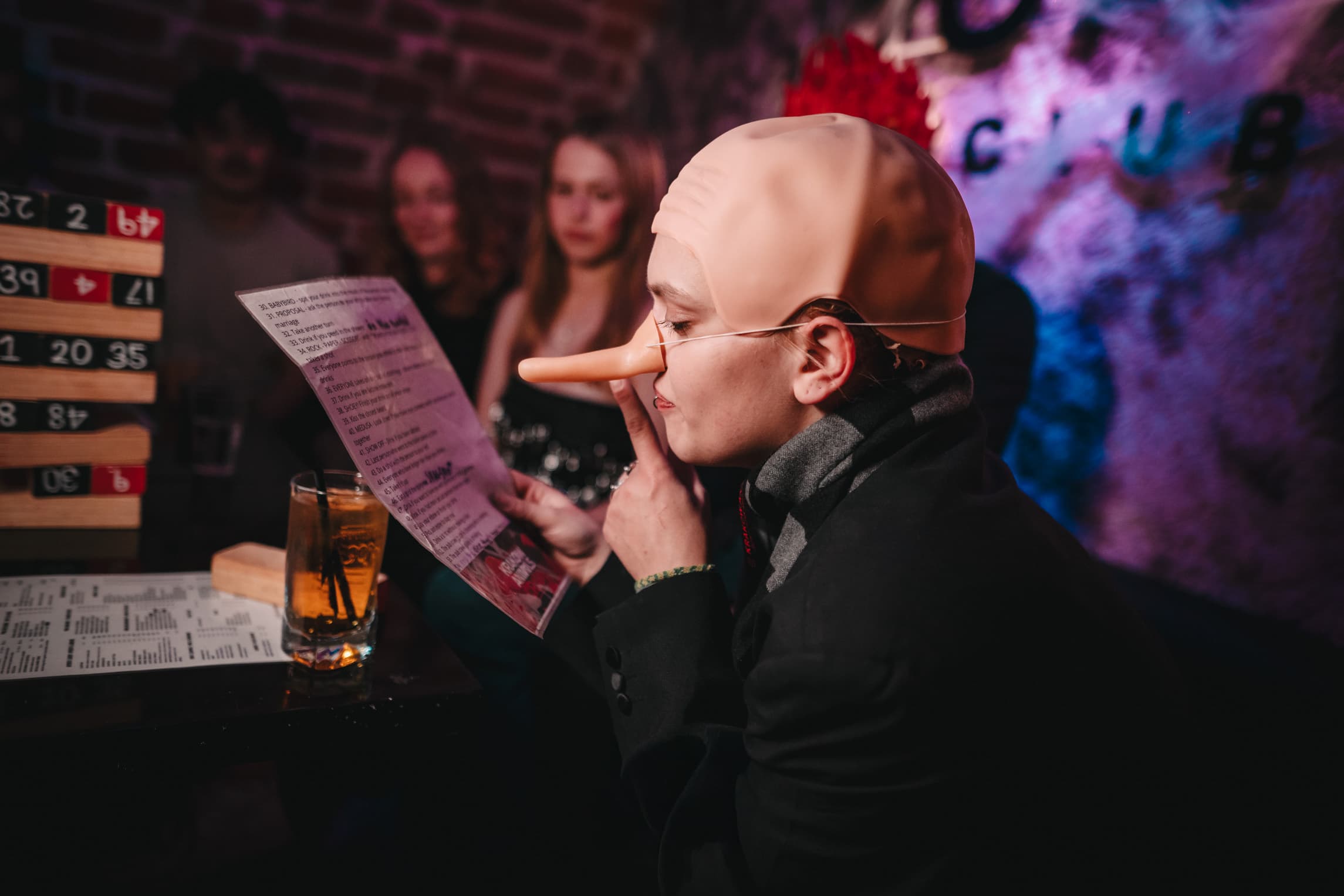 Costumed guest reading a party game card beside a drink